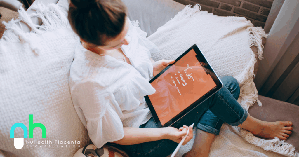 “Pregnant woman in her second trimester writing a postpartum preparation checklist” “Placenta encapsulation booking included in second trimester prep” “Postpartum recovery essentials checklist for expecting mothers”